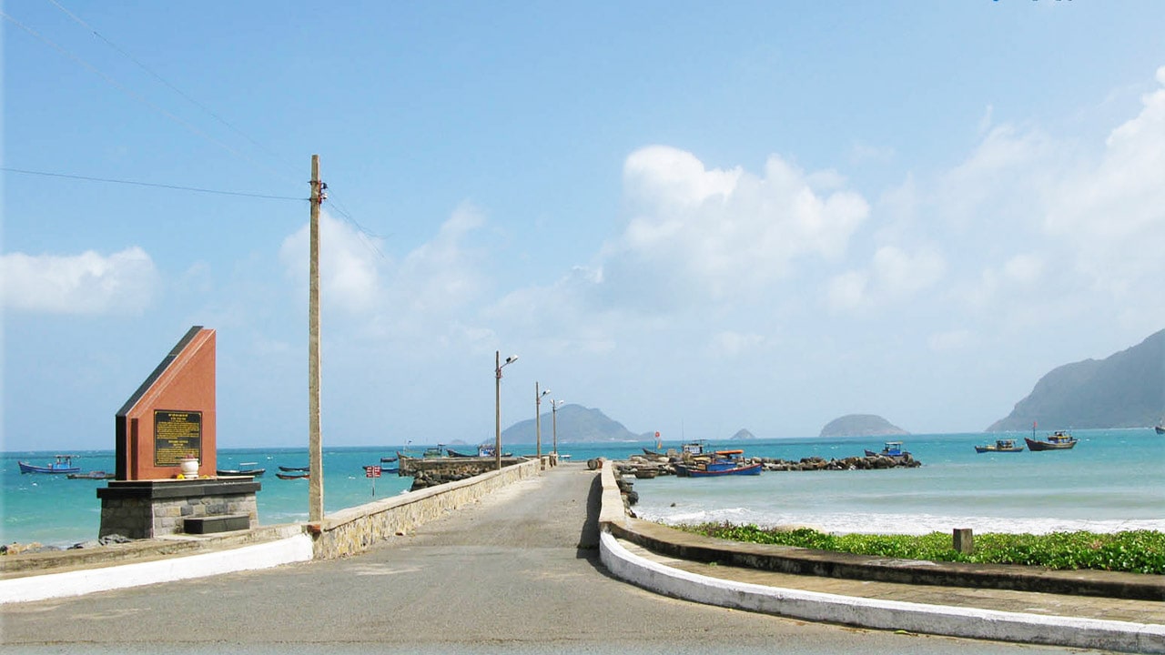 Lối bê tông dẫn ra Cầu tàu 914 ở Côn Đảo, bên cạnh bia di tích, phía trước là biển xanh, thuyền nhỏ và núi đảo xa bờ. – Kết luận